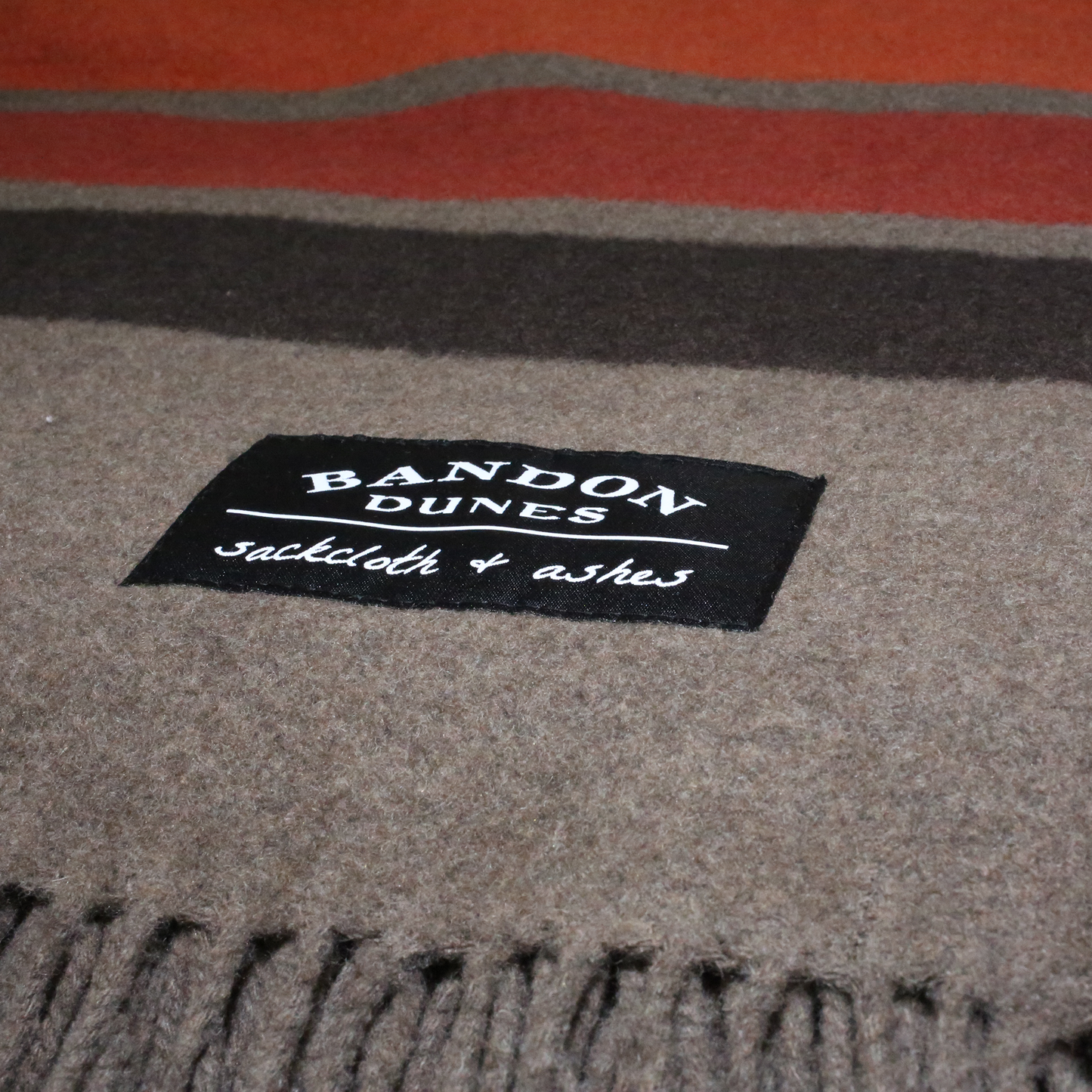 Brown blanket with dark brown, red, orange, and gold fall color stripes at top and bottom. Shows fringe and Bandon Dunes patch.