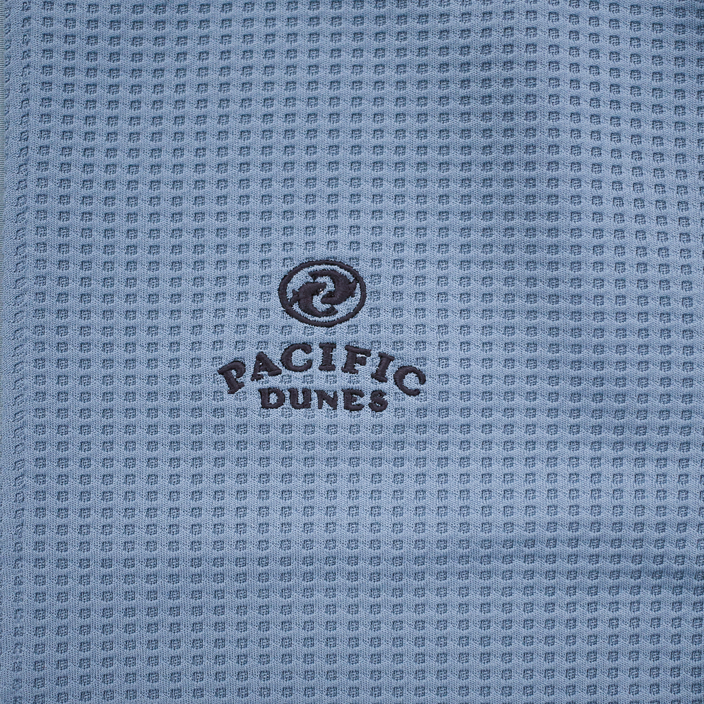 Close up of light blue waffle-knit fabric with embroidered Pacific Dunes logo.
