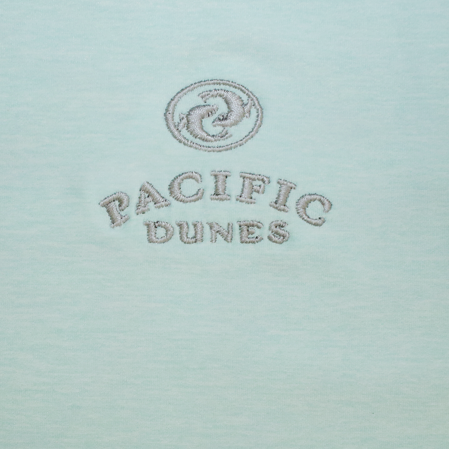Close up mint green fabric with gray embroidered Pacific Dunes logo.