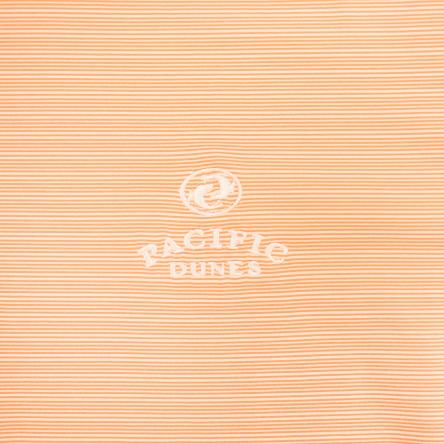 Close up striped light orange fabric with embroidered white Bandon Dunes logo. 