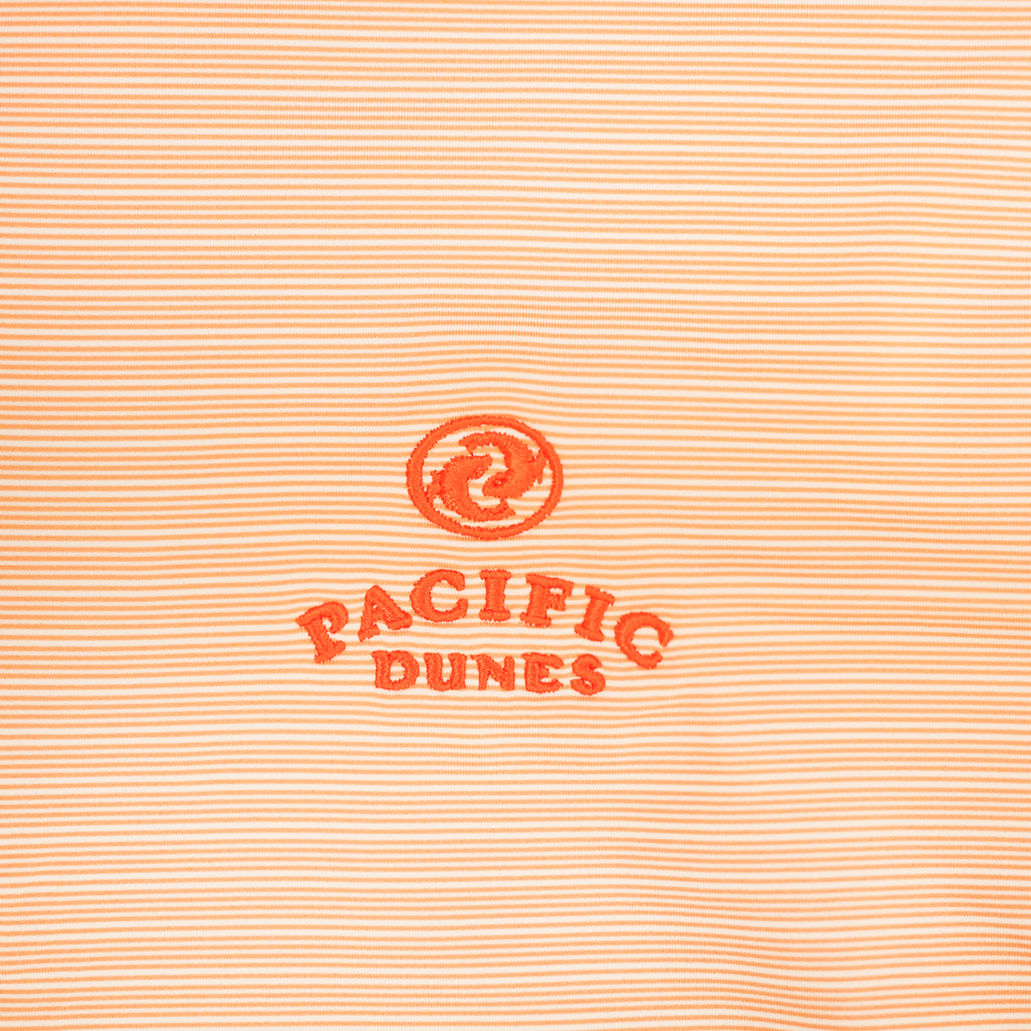Close up striped light orange fabric with embroidered orange Bandon Dunes logo. 