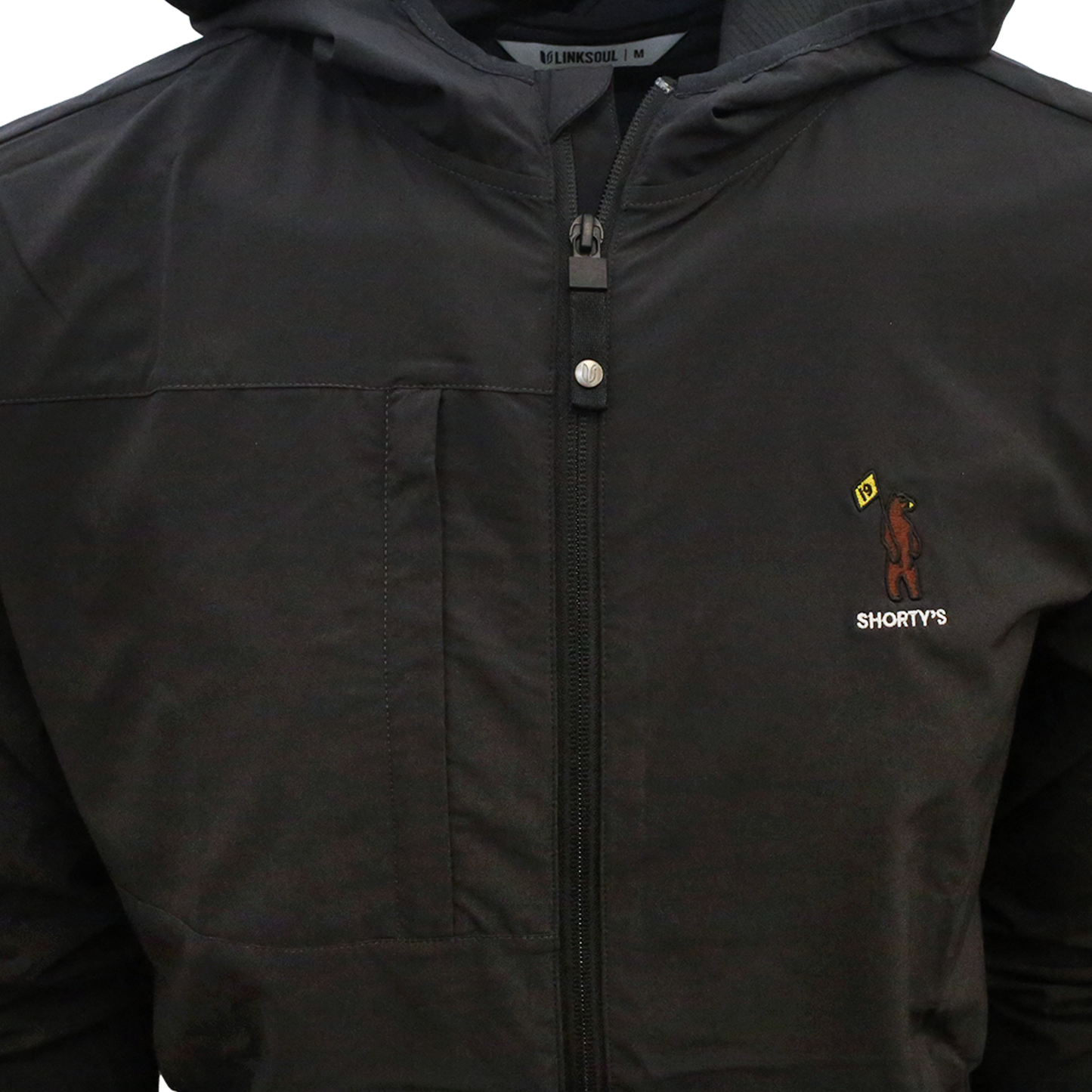 Close up of black lightweight full zip jacket with Shorty's bear logo embroidered on the left chest. 