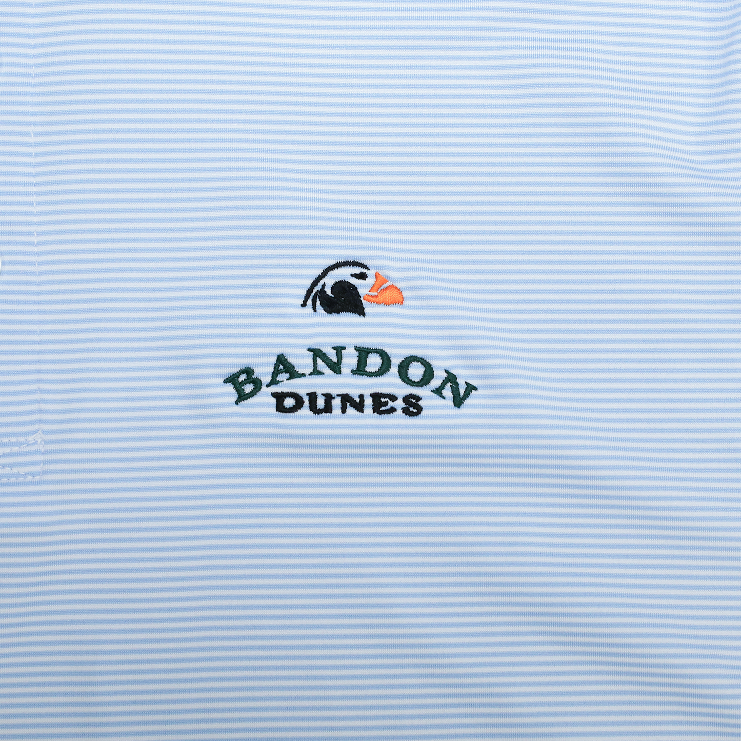 Close up of micro striped blue polo fabric and embroidered Bandon Dunes logo.