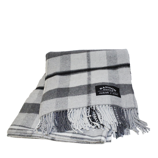 Blanket with gray, charcoal and black plaid design shows fringe and black Bandon Dunes patch.